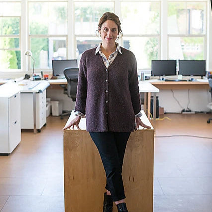 woman wearing the go-to cardigan in dark plum leaning on a wooden desk in an office setting