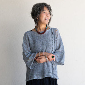 Woman wearing a gray sweater and black skirt against a white wall
