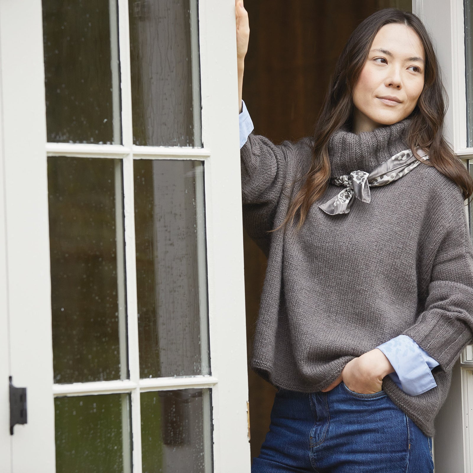 Woman wearing a gray sweater with a decorative brooch, standing indoors.