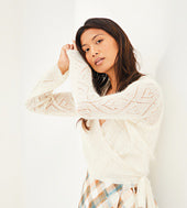 Woman wearing a Rowan Lupin, a white lace knit sweater against a plain background