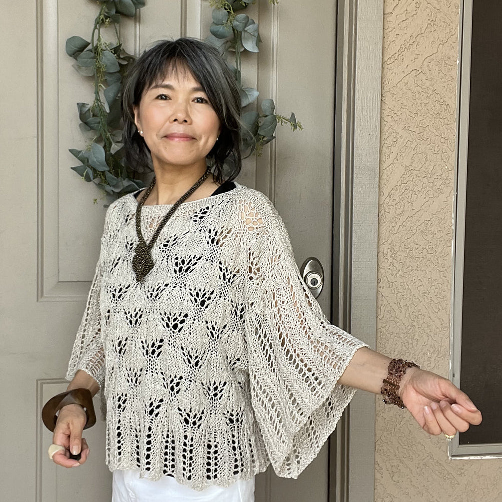 Woman standing in front of a door with a wreath, wearing a white lace top and white pants.